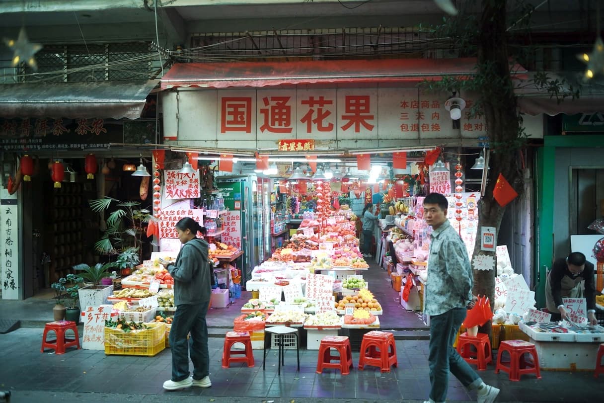 Shoppers passing a fruit and flower shop in a Guangzhou market street, China