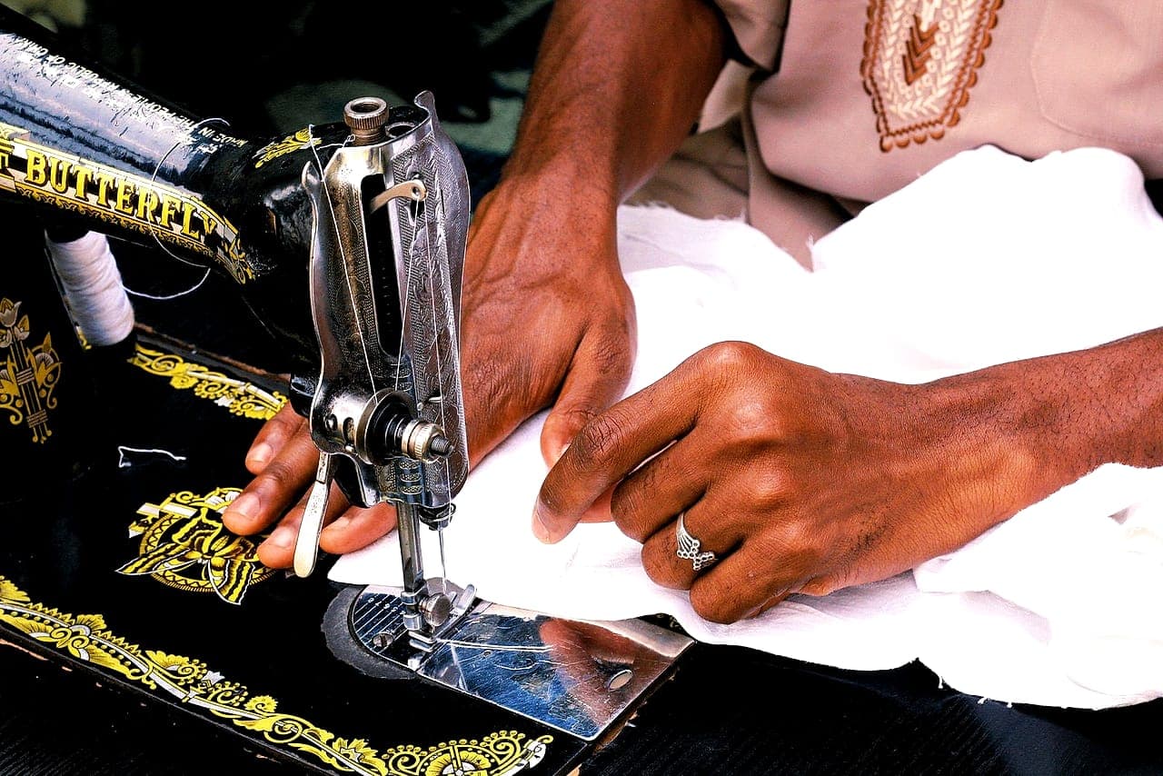 A tailor's hands guiding white fabric through a Butterfly sewing machine in Abuja, Nigeria